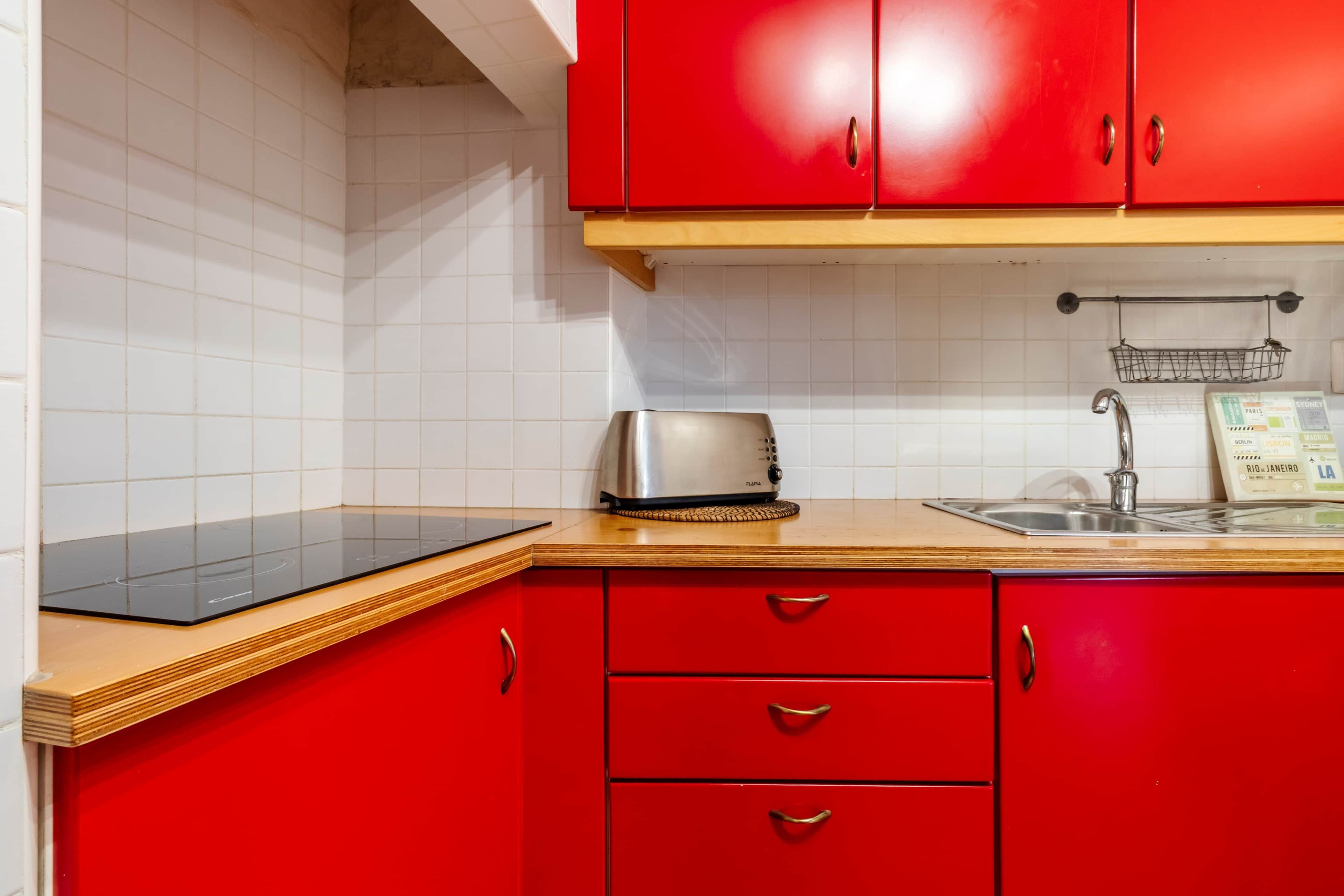 A kitchen with red cabinets, a black induction cooktop, a toaster, and a sink with a metal rack.