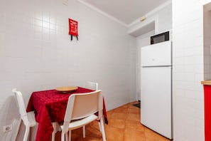 A compact kitchen with white tiled walls, a white refrigerator, a dining table with a red tablecloth, and white chairs. - Panorama View Apartment in Amazing Viewpoint (Lisbon)