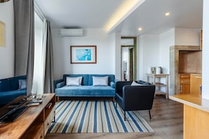 A modern living room with a sofa, a coffee table, a striped rug, a black chair, and a kitchen area with wooden cabinets. - Lisbon Panorama View Apartment (Lisbon)