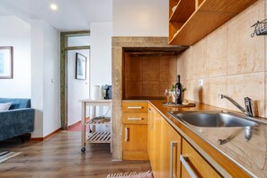 A modern kitchen with wooden cabinets, a stainless steel sink, and a small island with a wine bottle and glass. - Lisbon Panorama View Apartment (Lisbon)