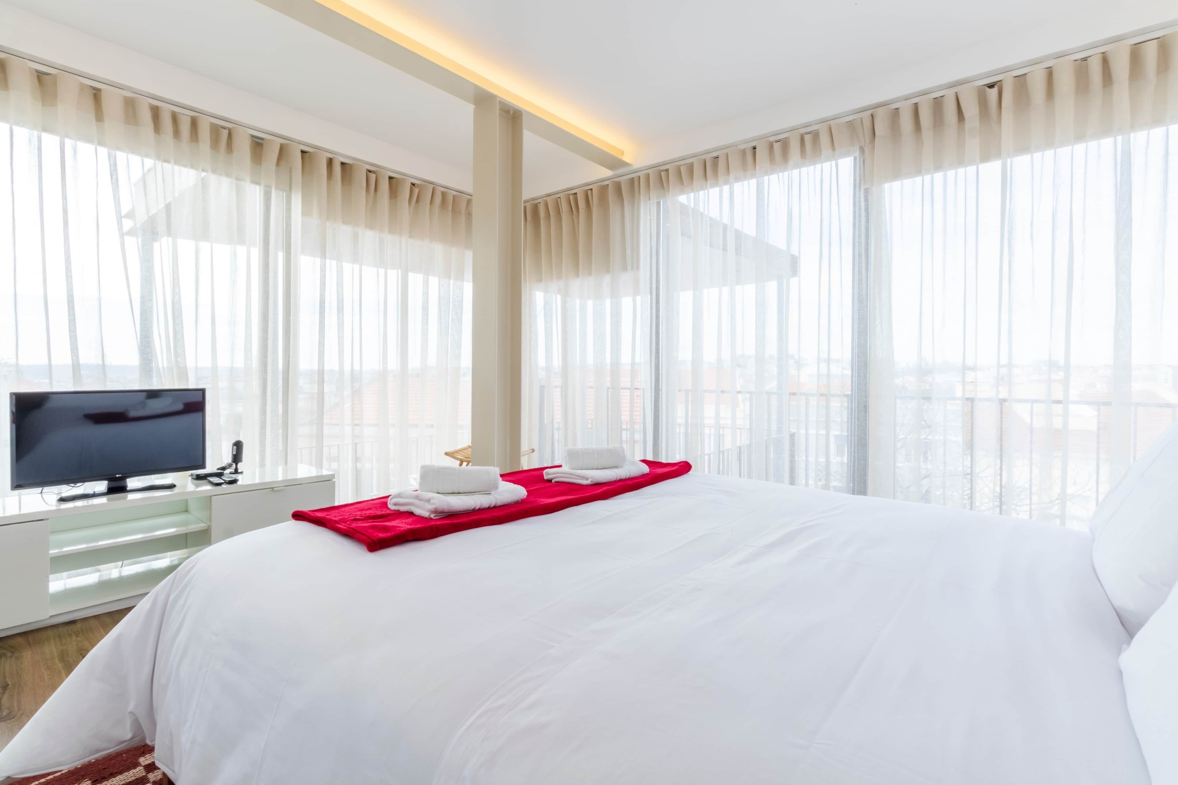 A hotel room with a large bed, a television, and a city view.