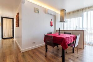 A dining area with a table set for two, a kitchen with a window, and a door with curtains. - Lisbon Panorama Apartment in Lisbon's Best Views (Lisbon)