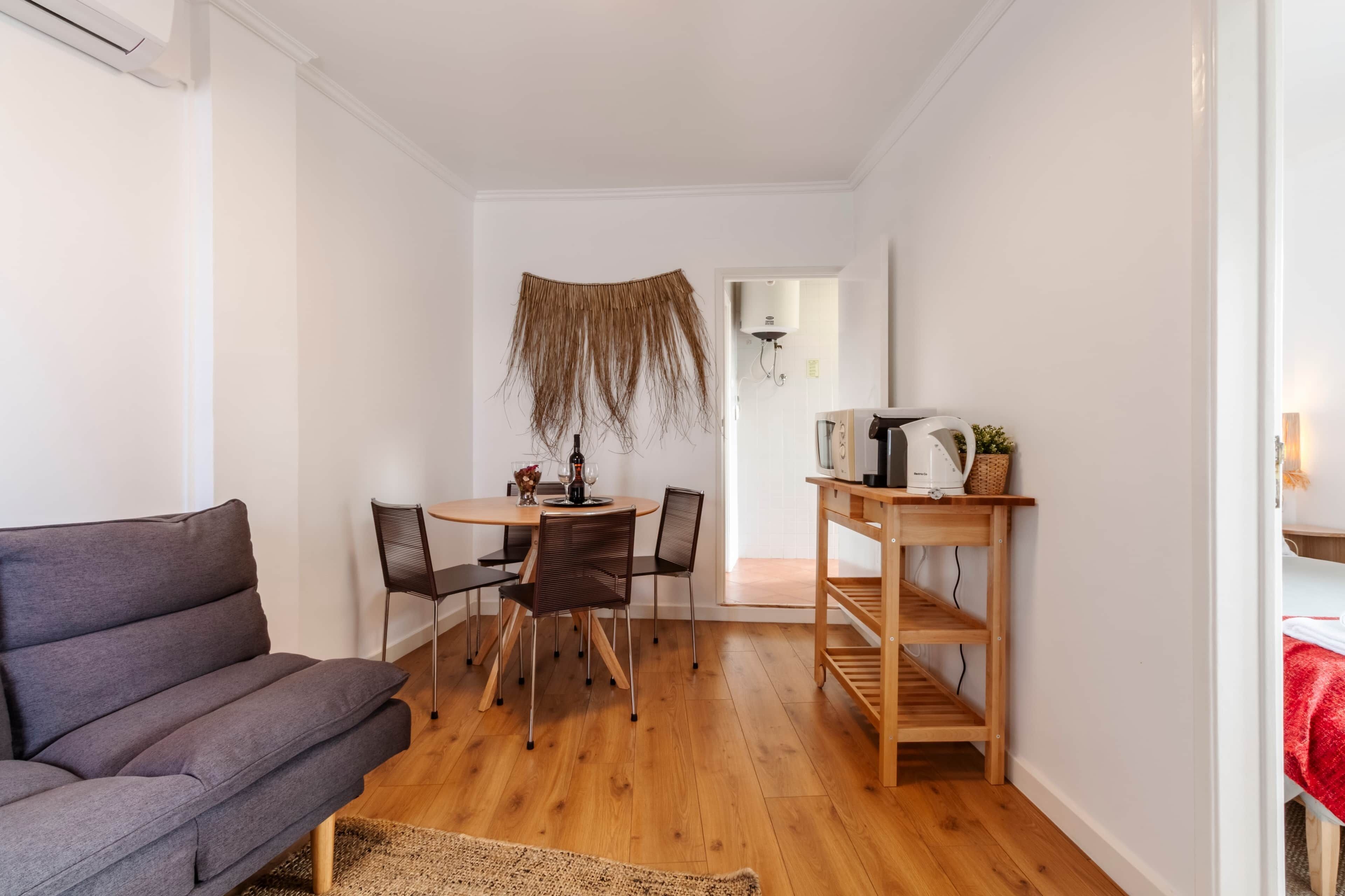 Ein Wohnzimmer mit einer Couch, einem Esstisch mit Stühlen, einem Holznachttisch und einer Wand-Klimaanlage.