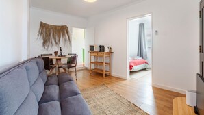 Ett modernt vardagsrum med en soffa, en matplats med bord och stolar, en tv på ett tv-bord och ett sovrum med en säng och gardiner.