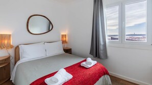 Ett hotellrum med en säng, en spegel, två sänglampor, ett fönster med gardiner och utsikt över stadsbilden.