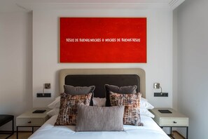 A hotel room with a bed, two bedside tables, a red wall art, and a nightstand with a lamp. - Príncipe Signature Residence (Madrid)