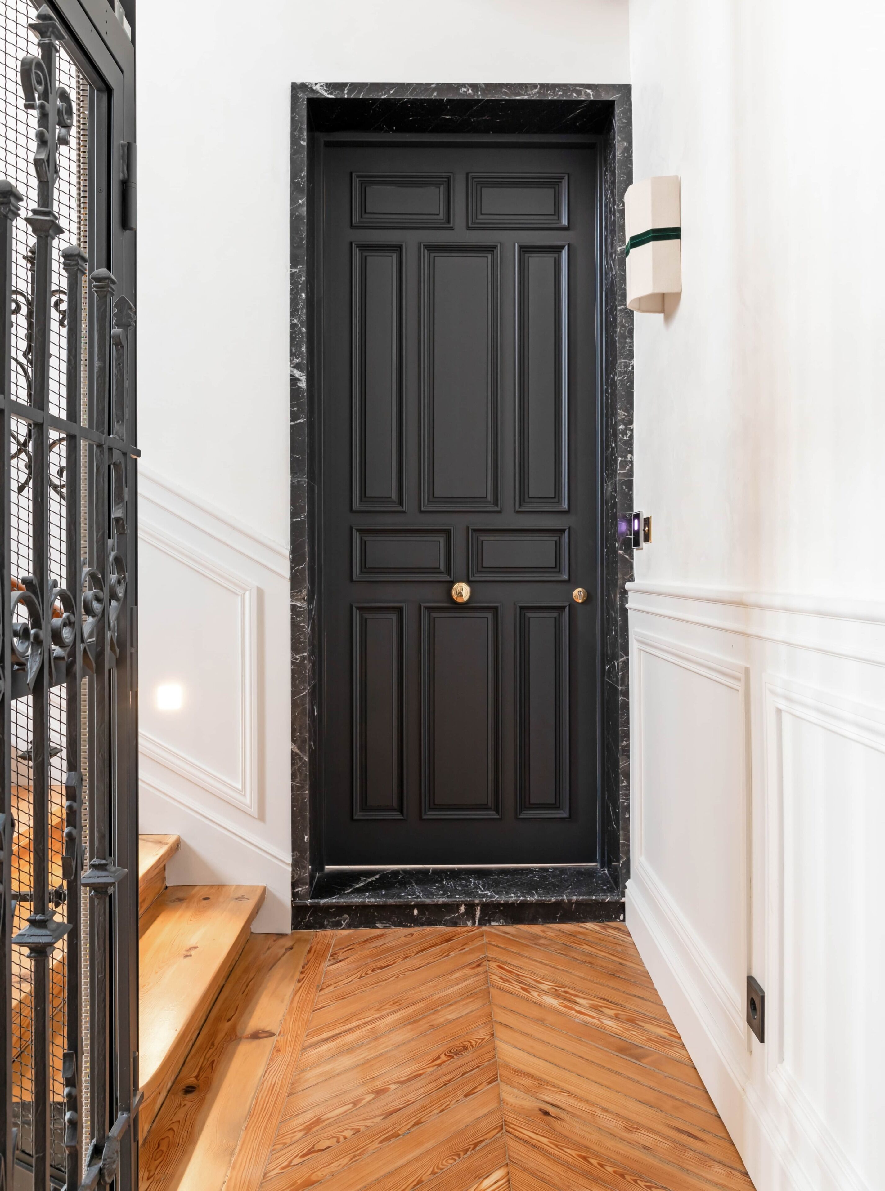Una puerta negra con pomo dorado, paredes blancas y un suelo de madera con patrón de espiga.