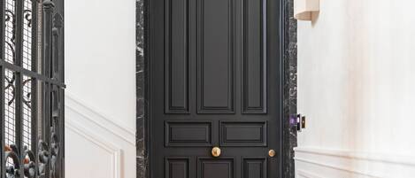 Una puerta negra con pomo dorado, paredes blancas y un suelo de madera con patrón de espiga.