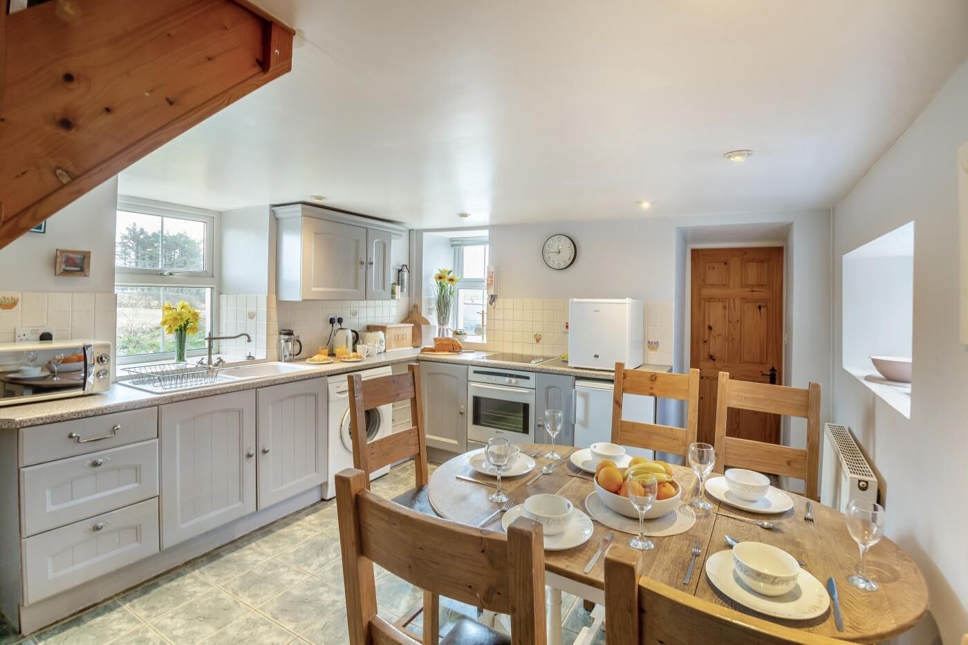 A modern kitchen with white cabinets, a dining table set for four, and a wooden ceiling.