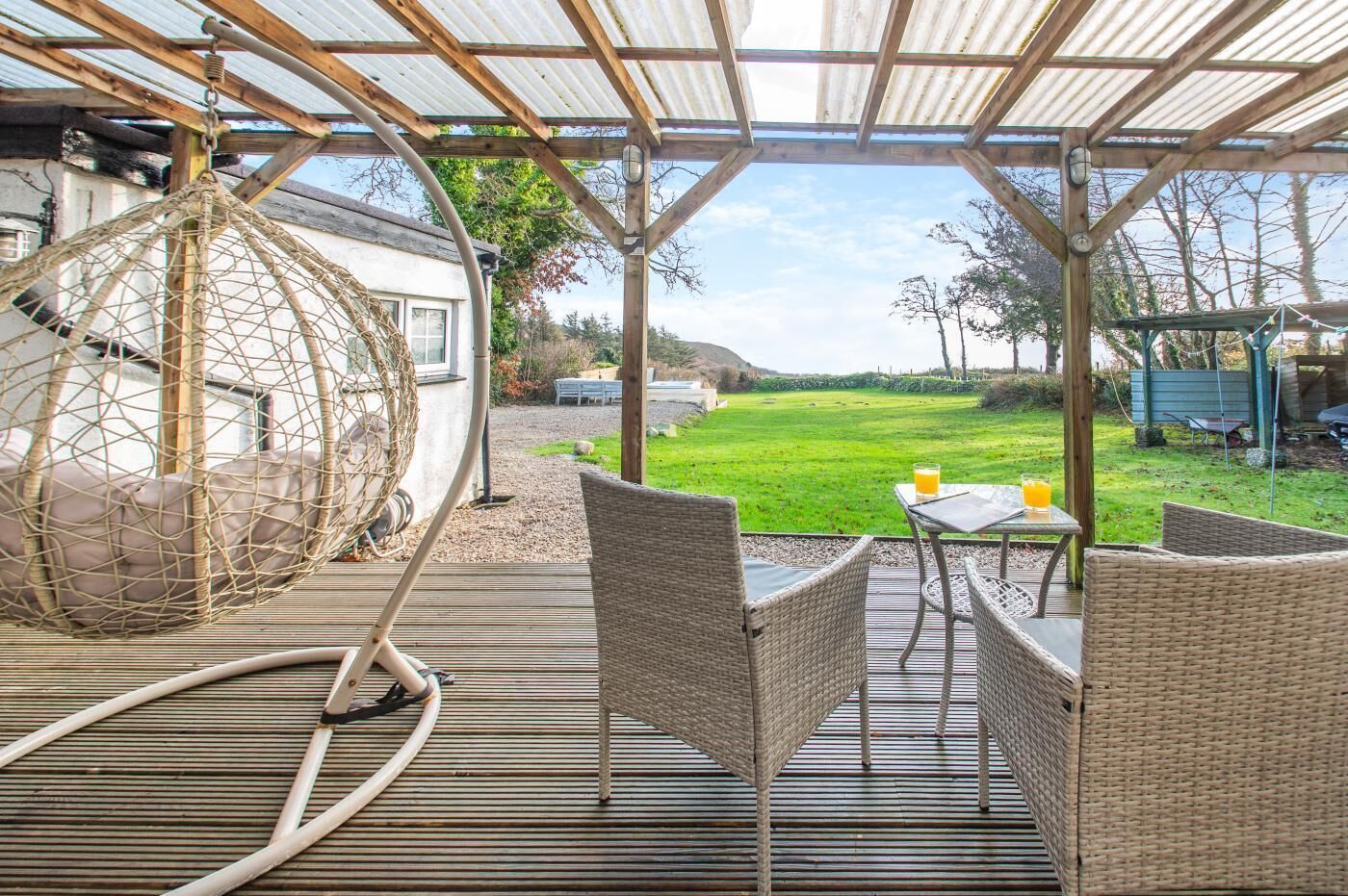 Un patio techado con muebles de mimbre, una silla colgante y vista a un jardín.