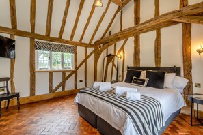 A bedroom with a large bed, wooden beams, a window with a zebra-patterned valance, and a bedside lamp. - 11 Bed in Stebbing (oc-p34450) (Stebbing Green)