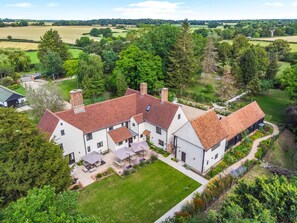 A large, white, two-story house with a red-tiled roof, surrounded by a well-maintained garden and a view of the countryside. - 11 Bed in Stebbing (oc-p34450) (Stebbing Green)