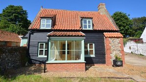 Una casa de dos pisos con techo de tejas rojas, una chimenea de ladrillo y un ventanal con marco blanco.