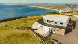 Une propriété située sur la côte, dotée d’un bâtiment aux lignes courbes, d’une terrasse et offrant une vue sur la mer et une ville lointaine.