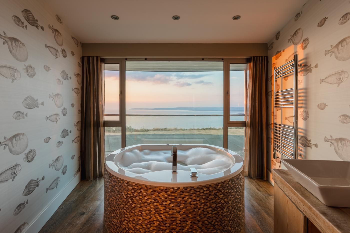 A bathroom with a large bathtub, a window with a view of the sea, and a shower area.