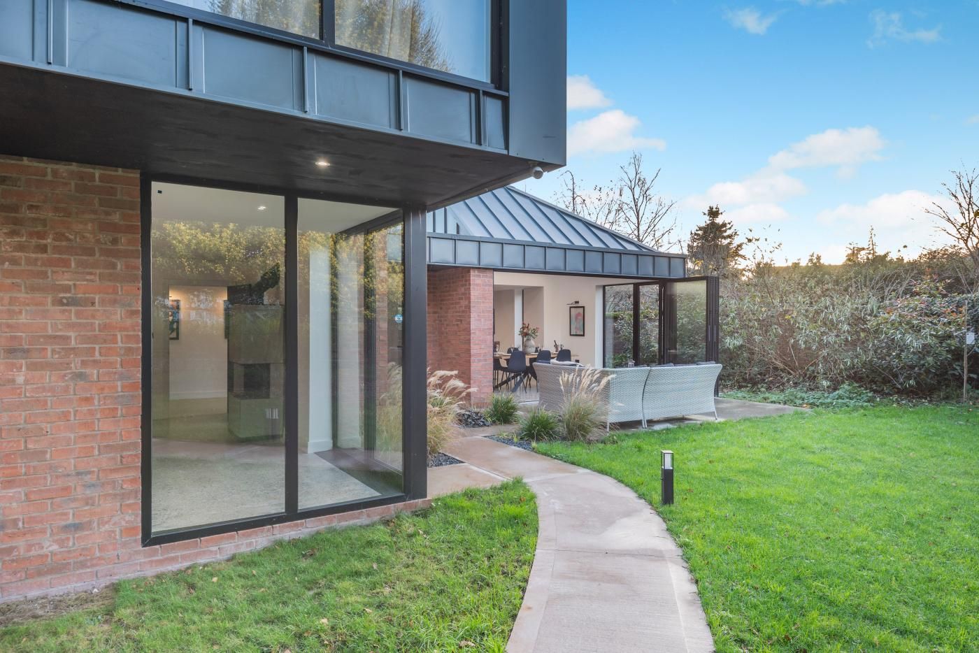 Une maison moderne avec de grandes fenêtres en verre, une façade en briques et une pelouse bien entretenue.