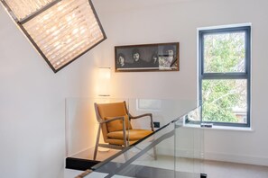A modern interior with a glass staircase, a framed artwork, a chair, and a window with a view of greenery. - 3 Bed in Leominster (oc-w34380) (Leominster)