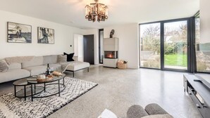 Een moderne woonkamer met een bank, salontafel, open haard en grote ramen.