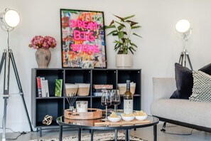 A modern living room with a bookshelf, a sofa, a coffee table with snacks and wine glasses, and a motivational poster. - 3 Bed in Leominster (oc-w34380) (Leominster)
