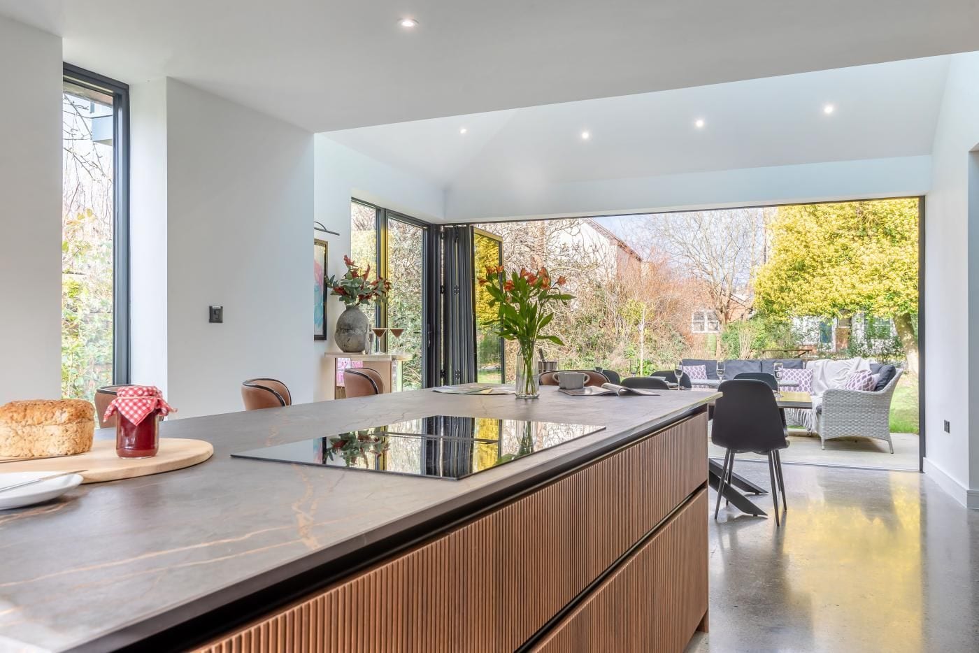 A modern kitchen with a central island, large windows, and a view of the garden.