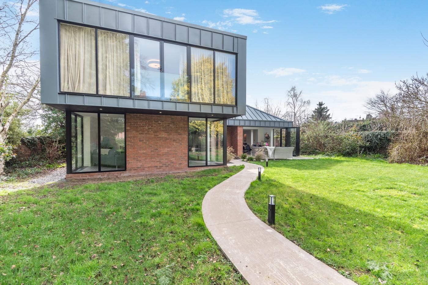 Une maison moderne à deux étages, avec une façade en briques, de grandes fenêtres et une pelouse bien entretenue.