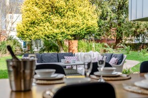 An outdoor dining area with a sofa and table set for a meal, surrounded by greenery and a tree. - 3 Bed in Leominster (oc-w34380) (Leominster)