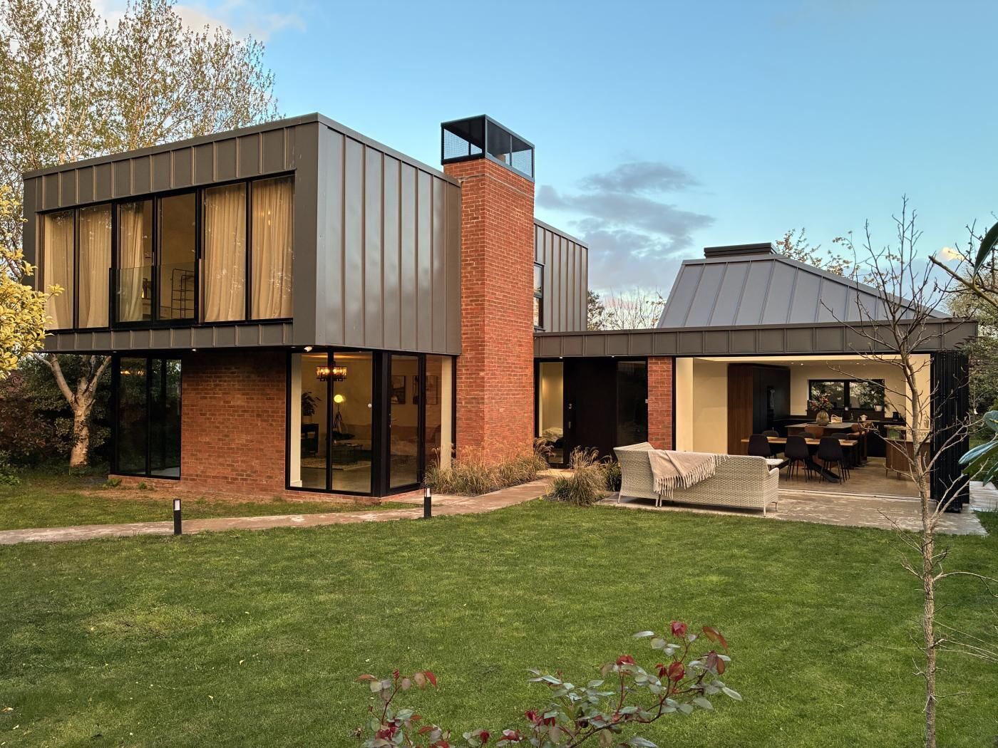 A modern two-story house with a brick facade, large windows, and a covered outdoor seating area.