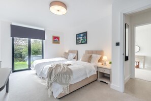 A modern bedroom with a large bed, bedside tables, a nightstand, a mirror, and a view of the outdoors. - 3 Bed in Leominster (oc-w34380) (Leominster)