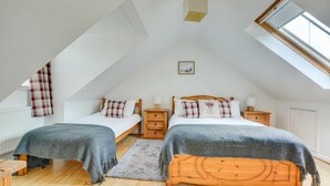A bedroom with two beds, a skylight, a wooden headboard, and a small bedside table with a lamp. - 2 Bed in Salhouse (oc-1250) (Salhouse)