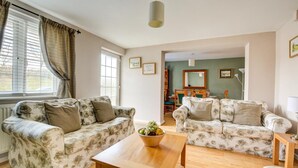 A living room with two floral-patterned sofas, a wooden coffee table, and a dining area with chairs and a table. - 2 Bed in Salhouse (oc-1250) (Salhouse)