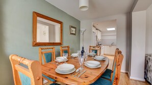 A dining area with a wooden table, chairs, and a mirror on the wall. - 2 Bed in Salhouse (oc-1250) (Salhouse)