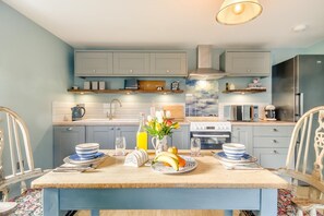 A kitchen with a dining table set for two, a stove, microwave, and refrigerator. - 1 Bed in Happisburgh (oc-b34458) (Happisburgh Common)