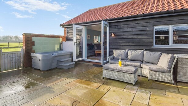 Une terrasse couverte avec un jacuzzi, des sièges d’extérieur et une vue sur la campagne.