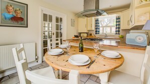 Una cocina con una mesa redonda de madera, sillas blancas, una estufa a gas y una radio antigua.