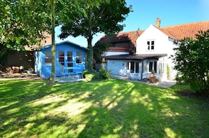 Ein Haus mit einem blauen Schuppen, ein weißes Haus und ein Garten mit Rasen und Bäumen.