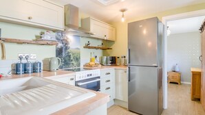 Une cuisine moderne équipée d’un réfrigérateur en acier inoxydable, d’un four encastré et d’une cuisinière à gaz. On y trouve des armoires en bois, un plan de travail avec une bouilloire et un grille-pain.