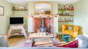 Un salon avec une cheminée en briques, un téléviseur, un fauteuil jaune et des étagères ornées d’objets décoratifs.