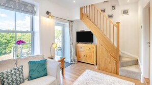 Ein Wohnzimmer mit einer Couch, einem Fernseher, einer Holztreppe und Blick auf Grünfläche.
