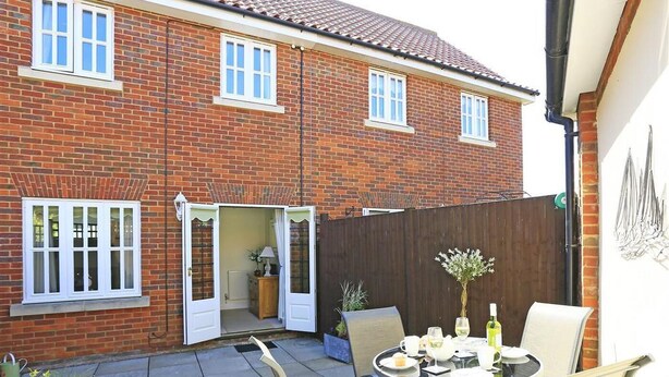 A brick house with a patio, a dining table with chairs, and a small garden area. - 3 Bed in Southwold (oc-kit) (Reydon)