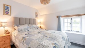 Ein Schlafzimmer mit Bett, Nachttischlampen, einem Nachttisch, einem Fenster mit Vorhängen und Wandbildern.