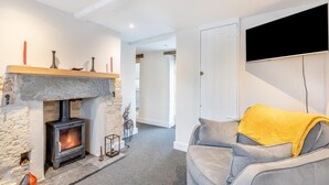 Ein gemütliches Wohnzimmer mit Kamin aus Stein, einer grauen Couch mit gelbem Überwurf und einem flachbildfernseher an der Wand.