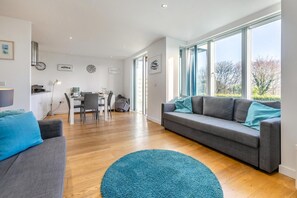 Ein modernes Wohnzimmer mit einem grauen Sofa, einem blauen Teppich und einem Essbereich mit Tisch und Stühlen.