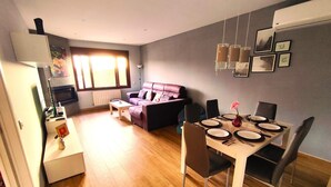 A dining area with a table set for four, a sofa, and a television in the background.