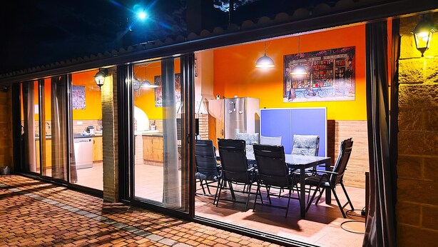 An outdoor seating area with a brick floor, tables, chairs, and a refrigerator.
