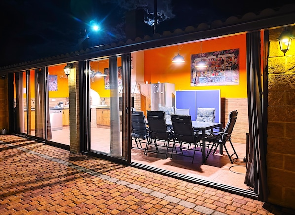 An outdoor seating area with a brick floor, tables, chairs, and a refrigerator.