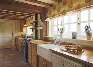 A kitchen with wooden cabinets, a stove, a sink, and a window with a view. - 5 Bed in Beccles (oc-ksf) (Henham)