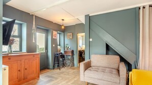 Een woonkamer met een bank, een gele stoel, een houten kast en een keuken in de achtergrond.