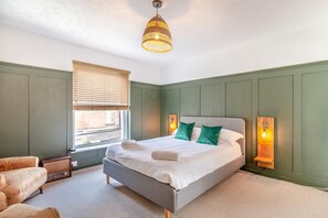 Une chambre à coucher avec un lit, une chaise, une fenêtre avec des stores et un luminaire suspendu.