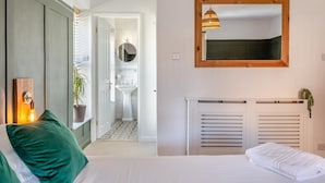 Een slaapkamer met een bed, nachtkastje, spiegel, radiator en uitzicht op de badkamer.