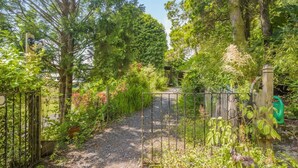 Un sendero en un jardín con una reja de metal, rodeado de abundante vegetación y árboles.